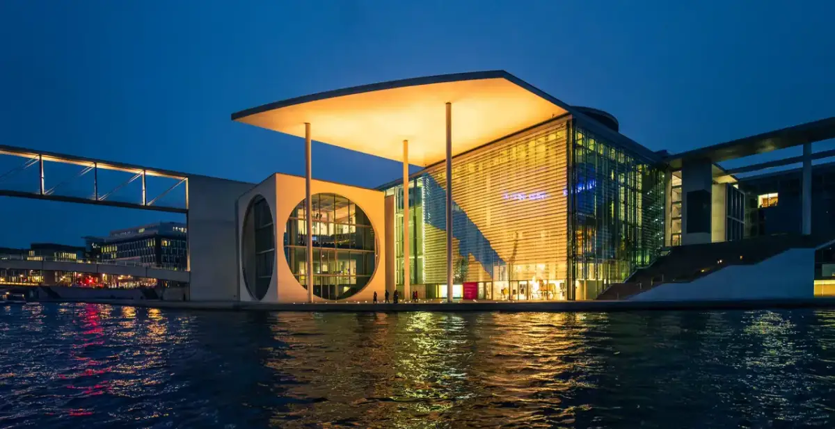 Nowoczesne muzeum sztuki w Berlinie, z charakterystycznym okrągłym oknem i przeszkloną fasadą, odbija się w wodzie.