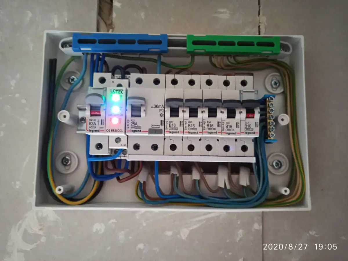 Widok wnętrza białej rozdzielni elektrycznej z bezpiecznikami i przewodami.