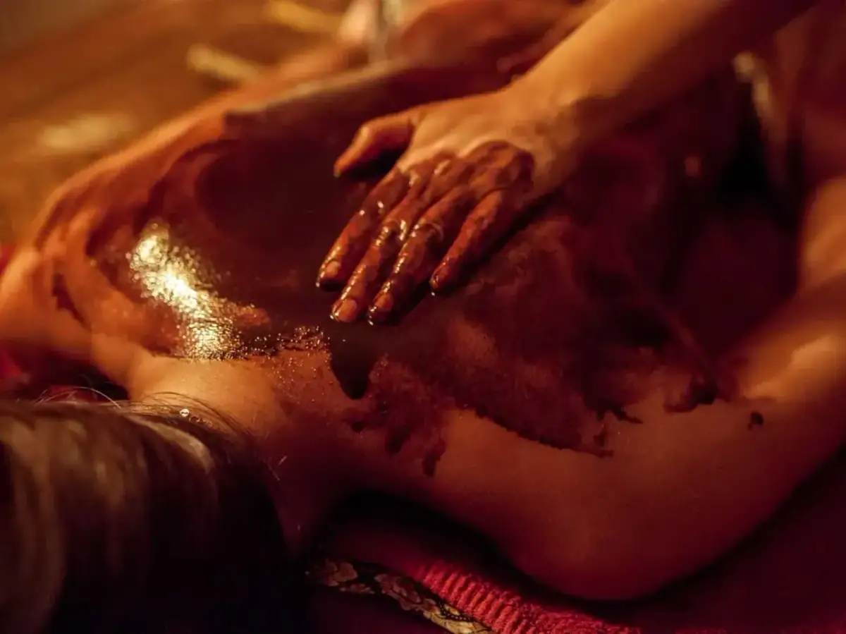 Dłoń masuje plecy pokryte czekoladą do masażu spa. Ciemna, błyszcząca masa rozpływa się na skórze, tworząc relaksującą atmosferę.