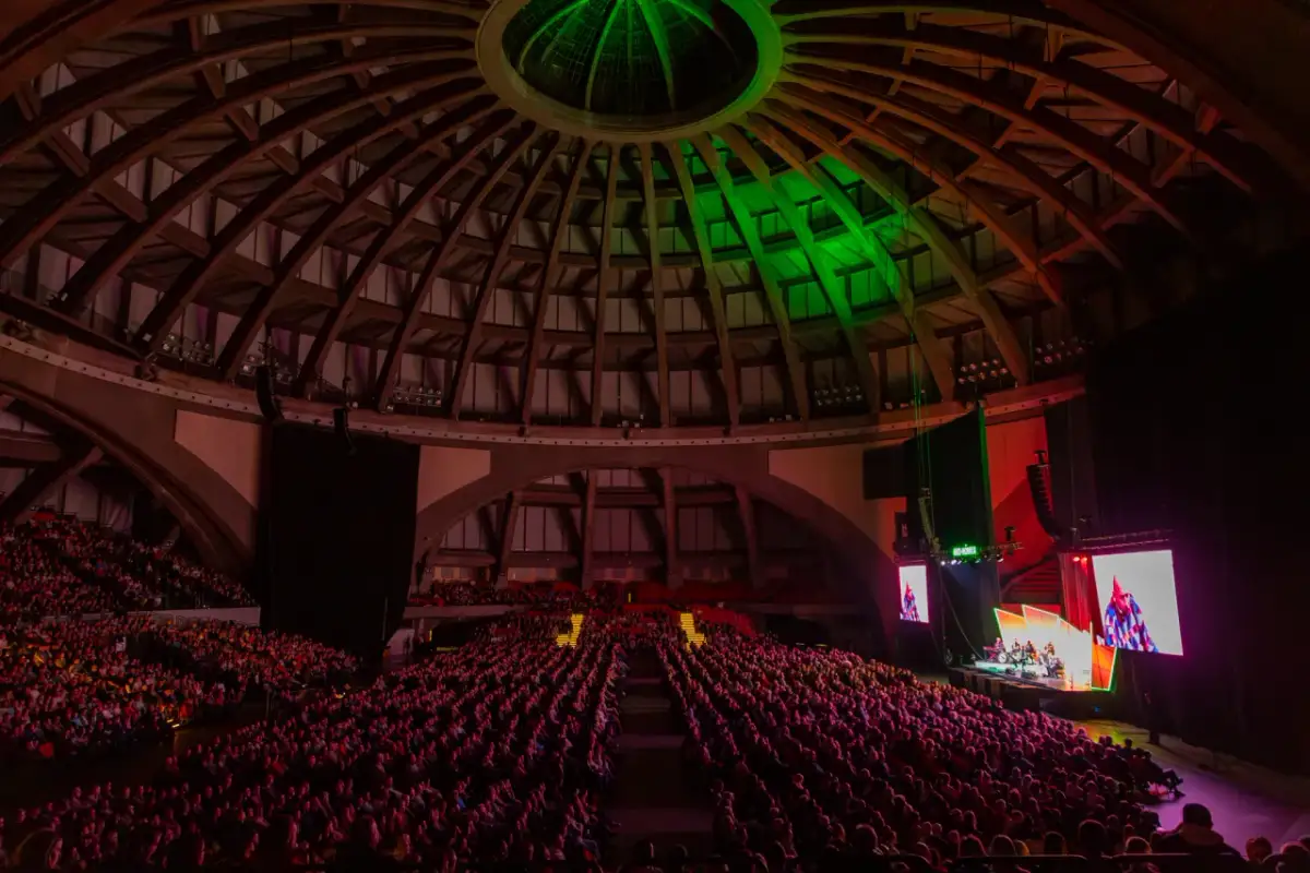 Ogromna widownia w Hali Stulecia czeka na występy kabaretu Neonówka. Zielone światła oświetlają kopułę.