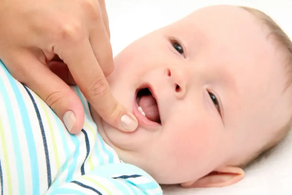 Dłoń rodzica delikatnie dotyka dziąsełka niemowlaka, pokazując pierwszy ząbek.