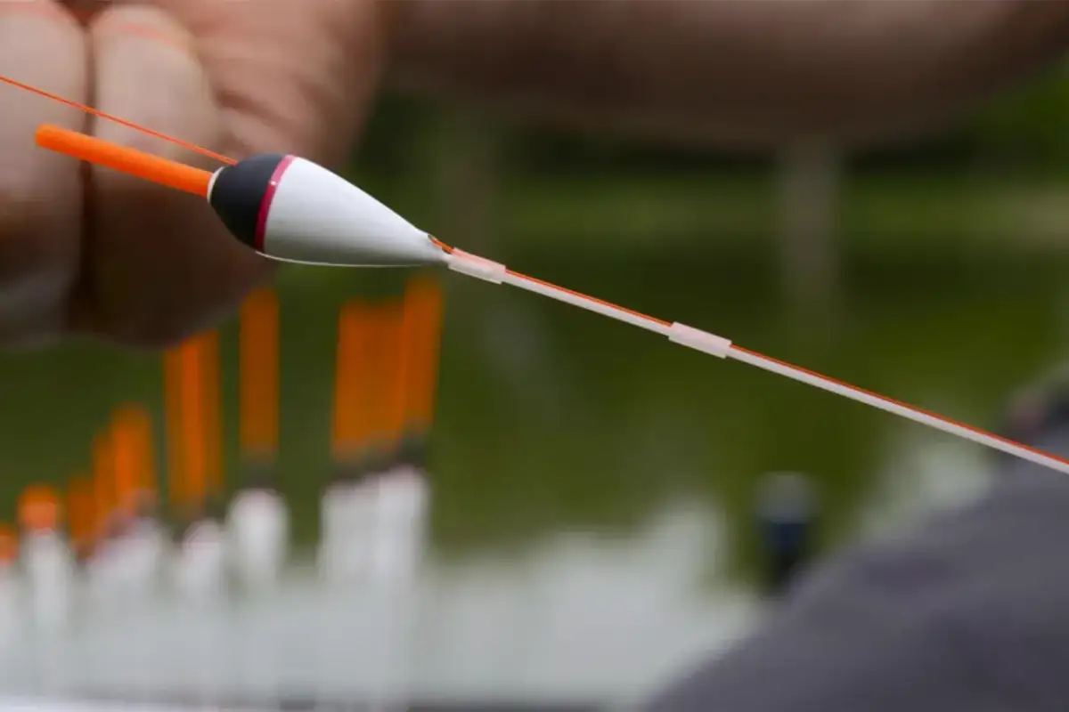 Zbliżenie na biało-czarny spławik wędkarski z pomarańczową antenką, trzymany na żyłce.