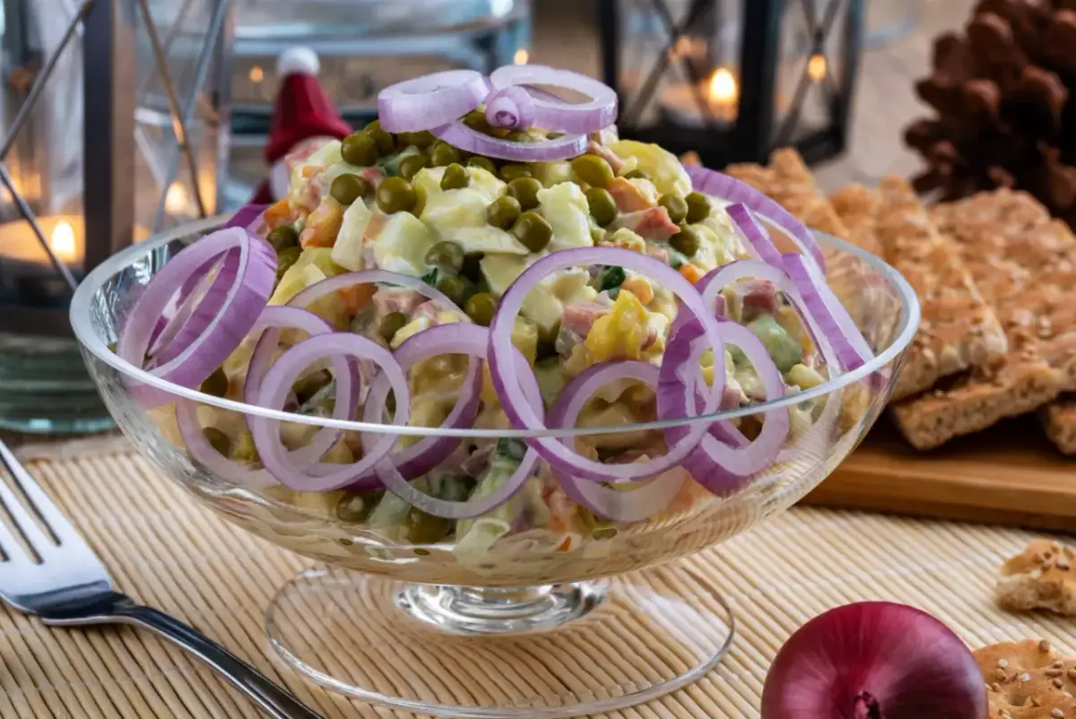 Pyszna sałatka jarzynowa, idealna na Wielkanoc, ozdobiona krążkami czerwonej cebuli. W tle widać świece i pieczywo.
