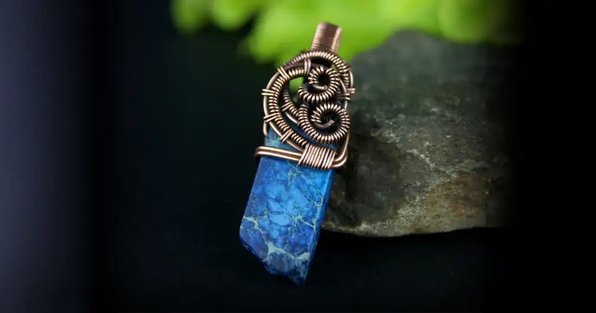 Wisior z niebieskim kamieniem i miedzianym drucianym owinięciem na kamieniu.