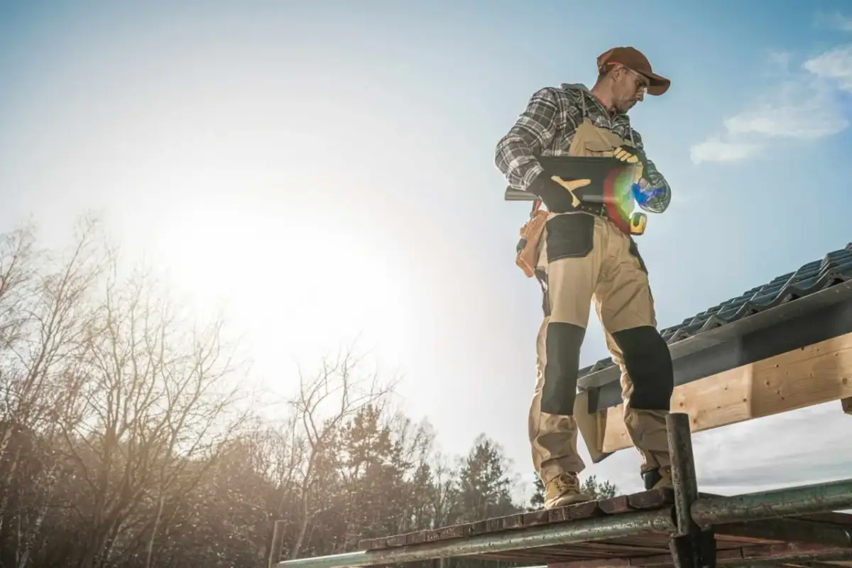 Dekarz na dachu, zastanawia się, ile zarabia blacharz dekarz. Słońce świeci, praca wre.