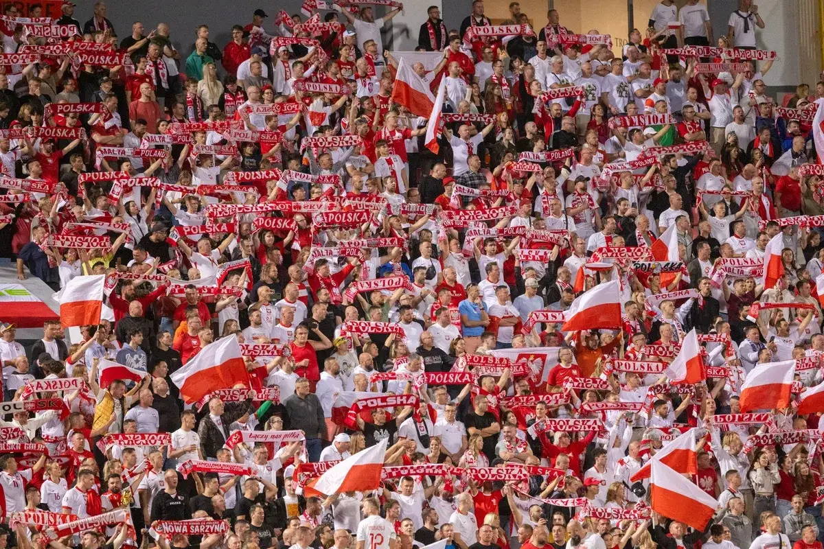 Tłum kibiców z szalikami "Polska" i flagami, emocjonujący doping podczas meczu, kiedy baraże o ekstraklasę.