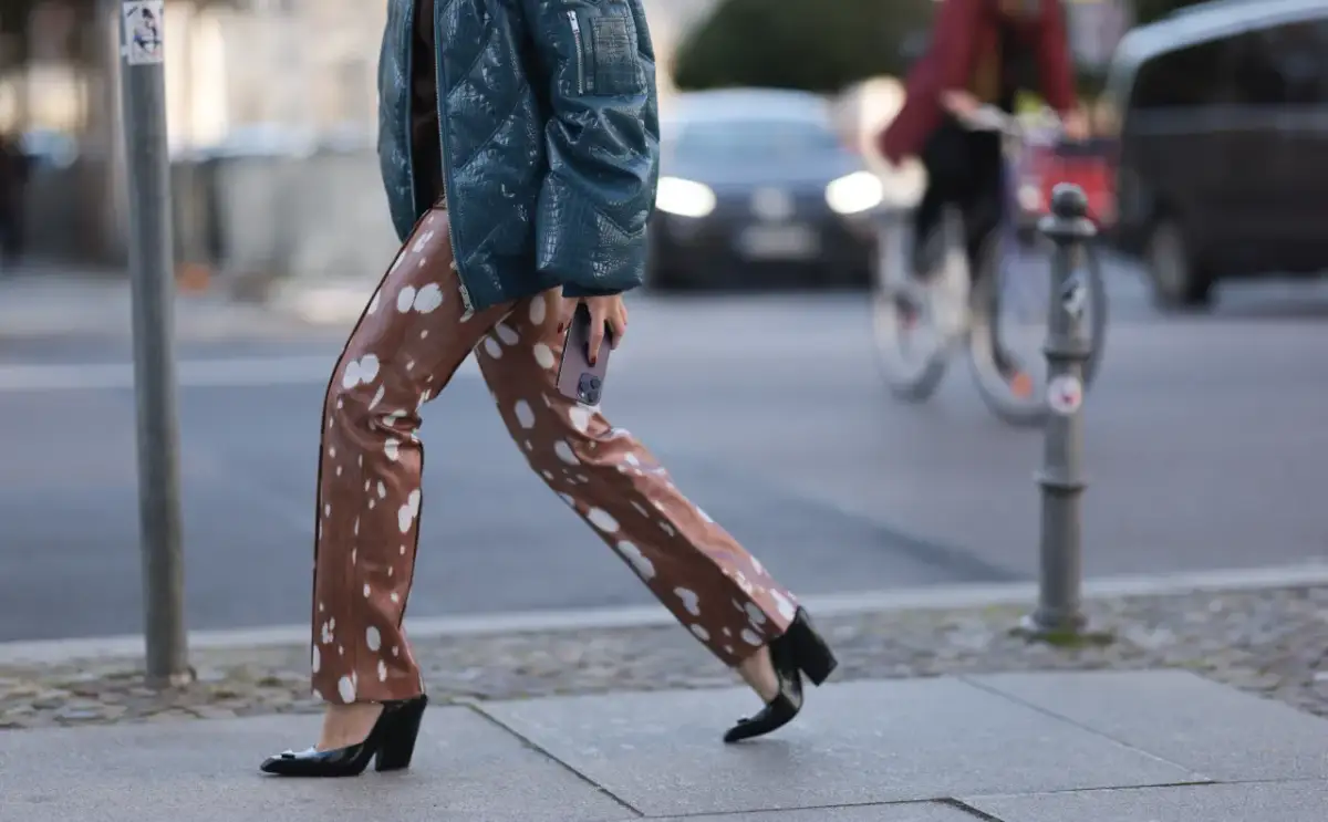 Kobieta w winylowych spodniach w cętki i błyszczącej kurtce idzie ulicą. Oto jak nosić winylowe spodnie, by wyglądać stylowo.