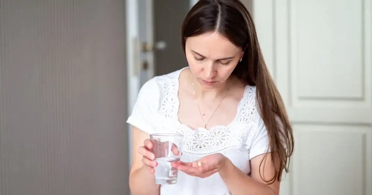 Kobieta trzyma szklankę wody i tabletkę na dłoni.