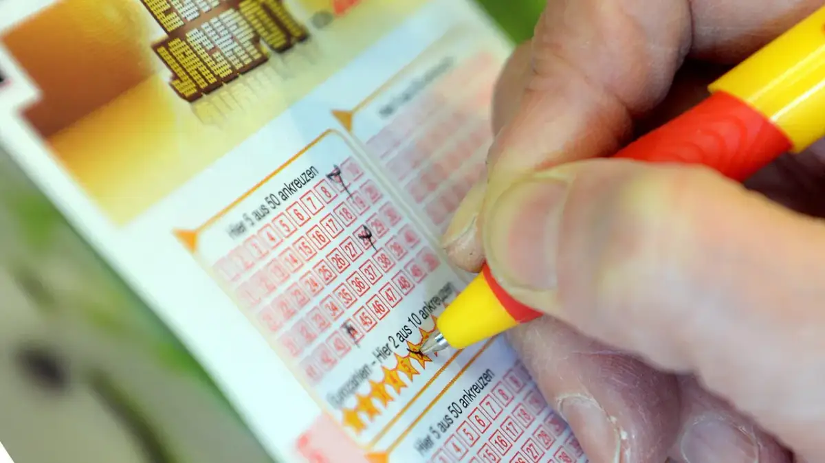 Dłoń z długopisem zaznacza liczby na kuponie lotto.