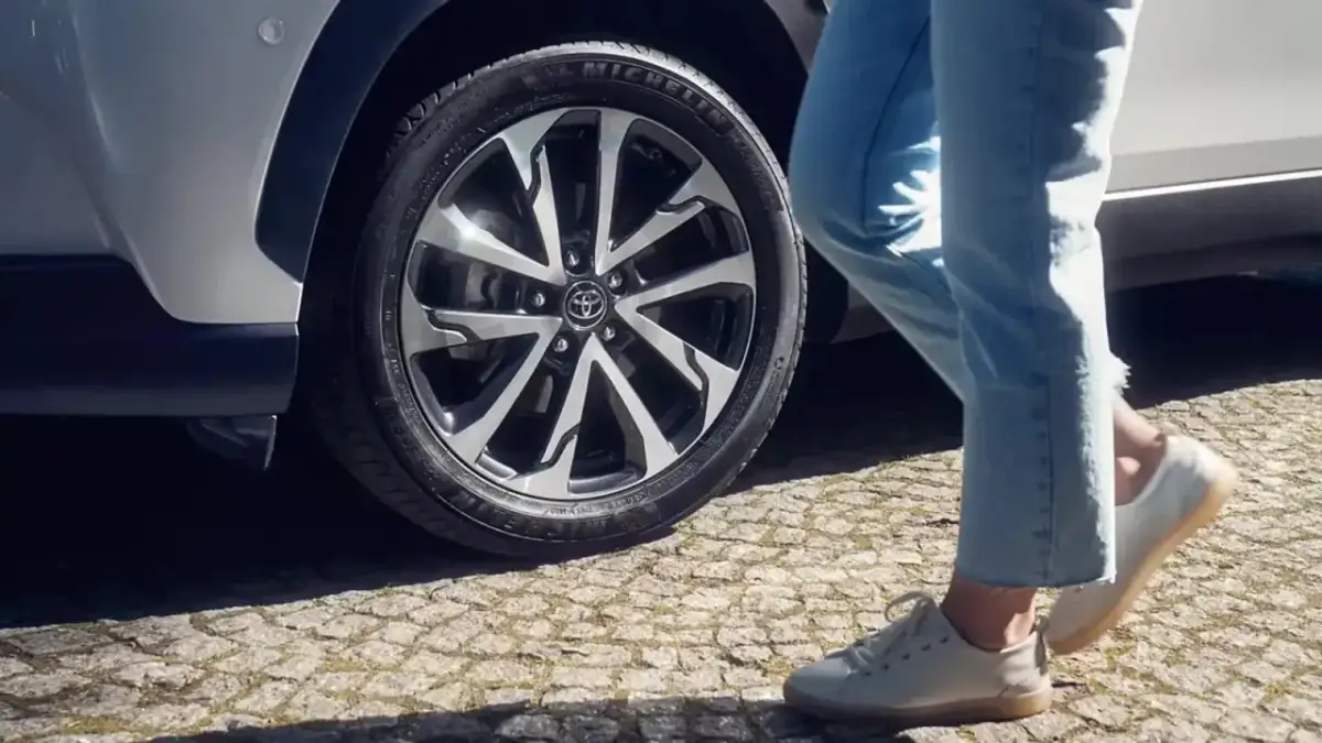 Osoba w jeansach i białych butach zbliża się do Toyoty Corolli. Dowiedz się, jak zresetować czujnik ciśnienia w oponach w tym modelu.