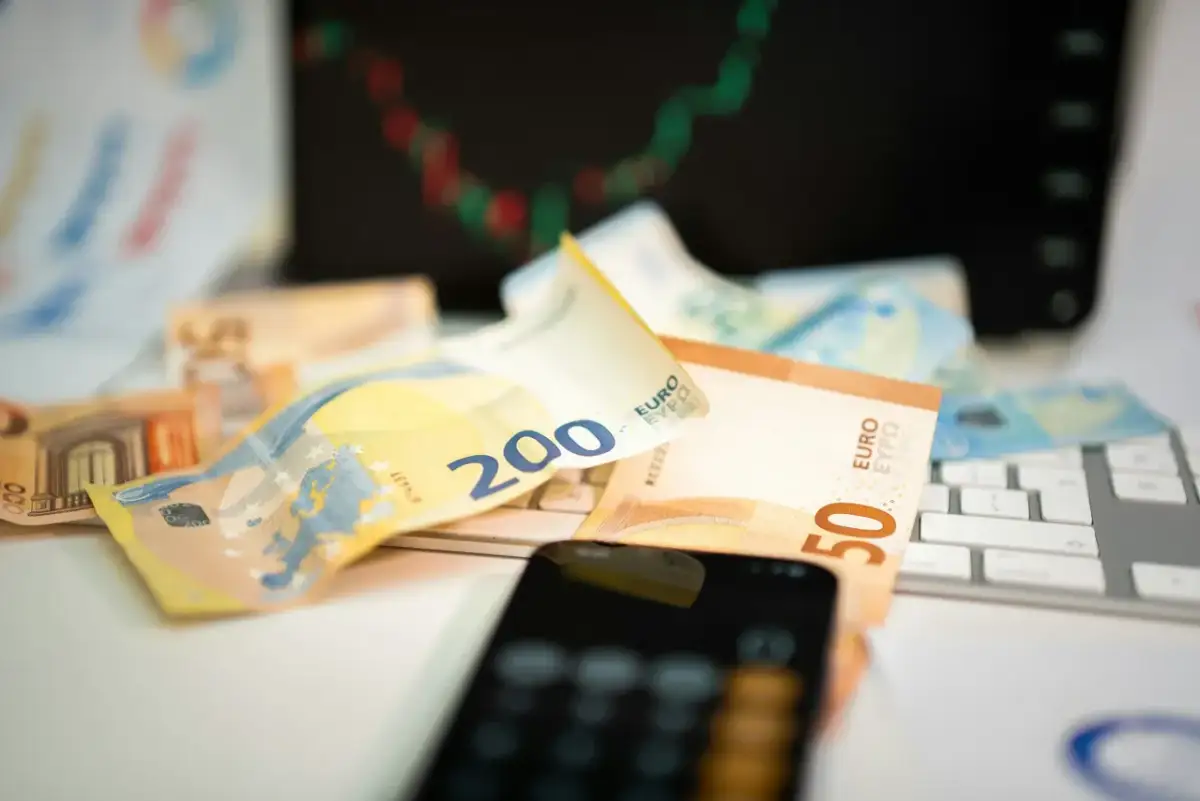 Euro banknoty na klawiaturze, telefon i wykres giełdowy sugerują inwestowanie w waluty.