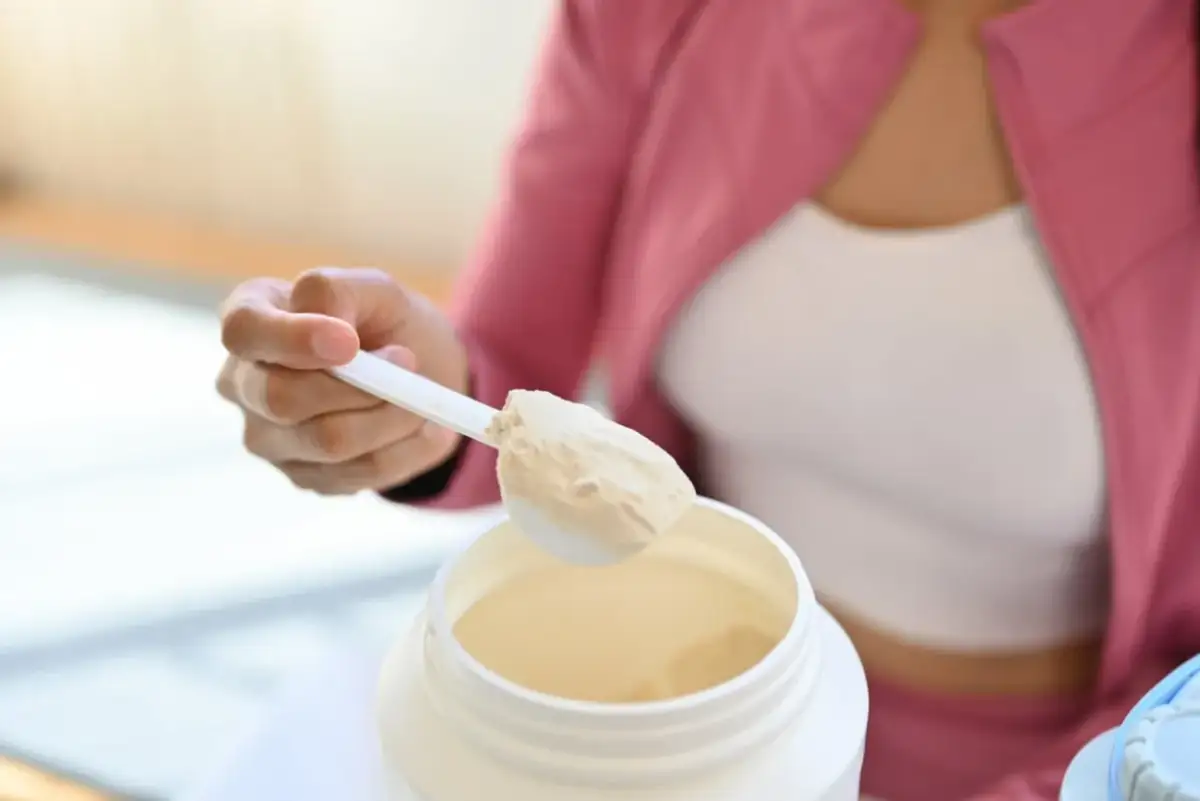 Dłoń nabiera miarkę białka w proszku. Kiedy pić białko przed czy po treningu? To pytanie zadaje sobie wiele osób aktywnych fizycznie.