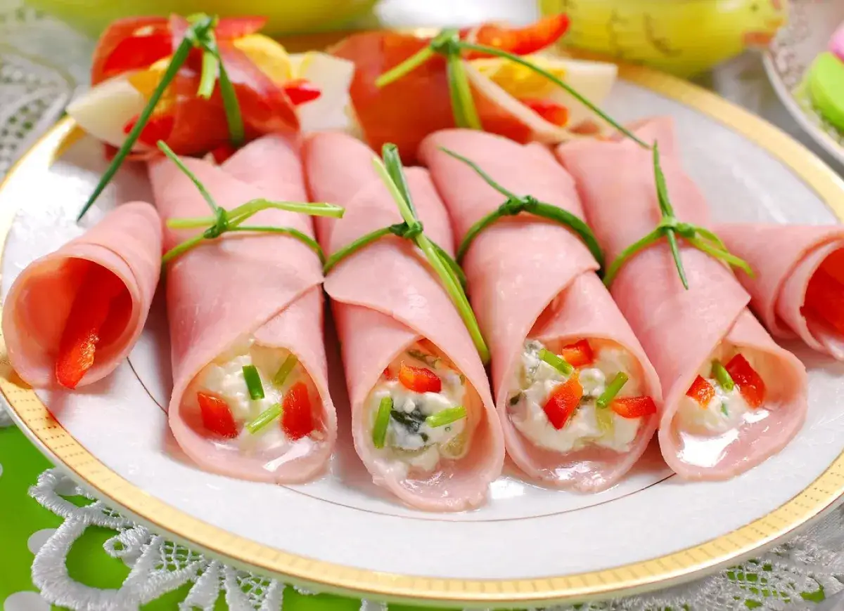 Roladki z szynki z kremowym nadzieniem i papryką, ozdobione szczypiorkiem. Idealna przekąska na przyjęcie.
