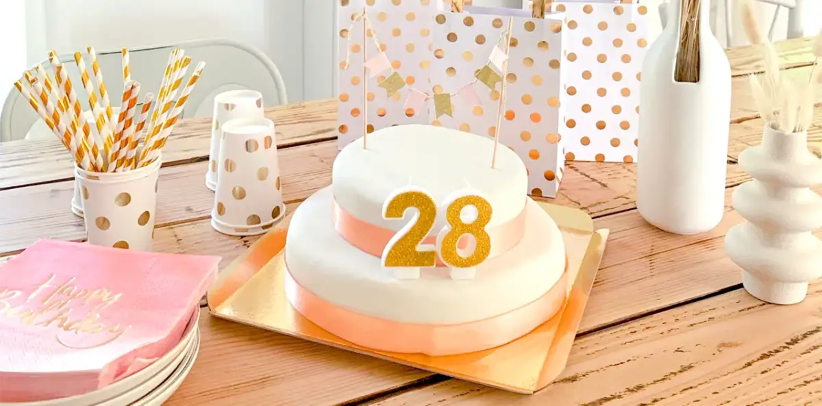 Tort urodzinowy z cyframi 28, ozdoby i prezenty na drewnianym stole.