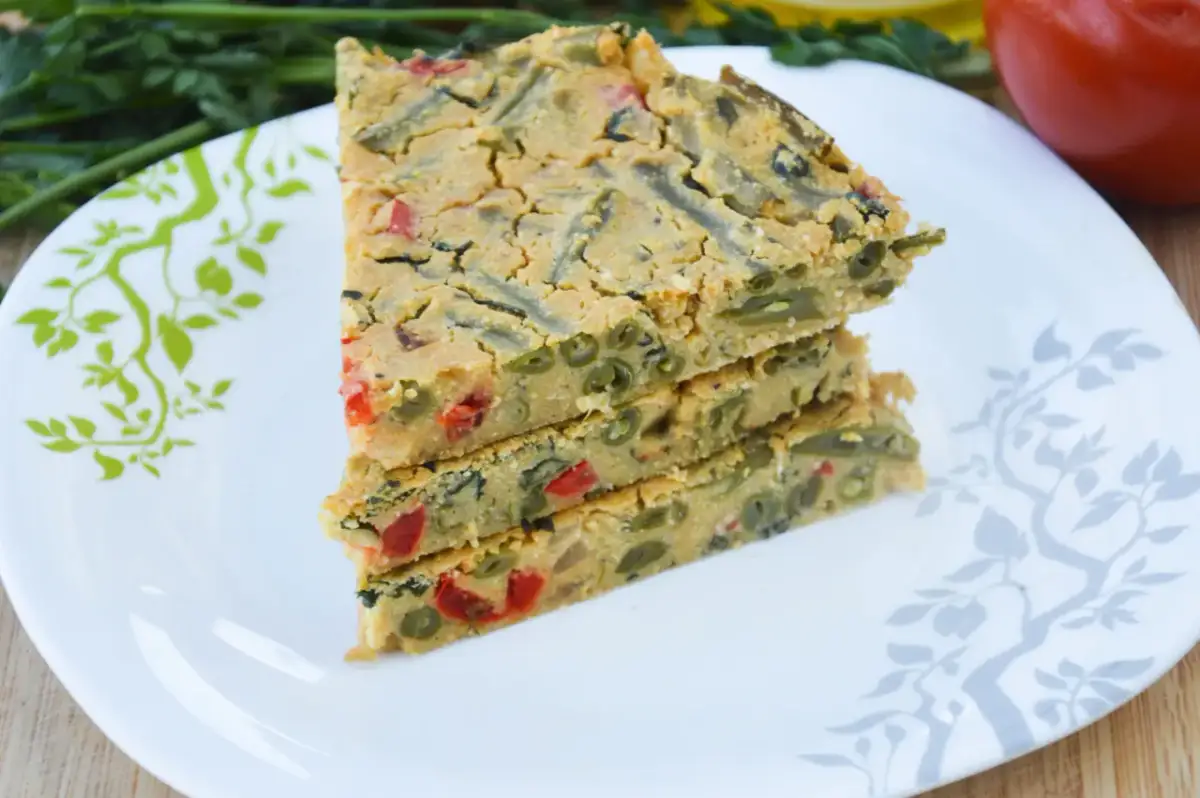 Pyszna wege kolacja: kawałki zapiekanki z fasolką szparagową i papryką na talerzu z zielonymi gałązkami.