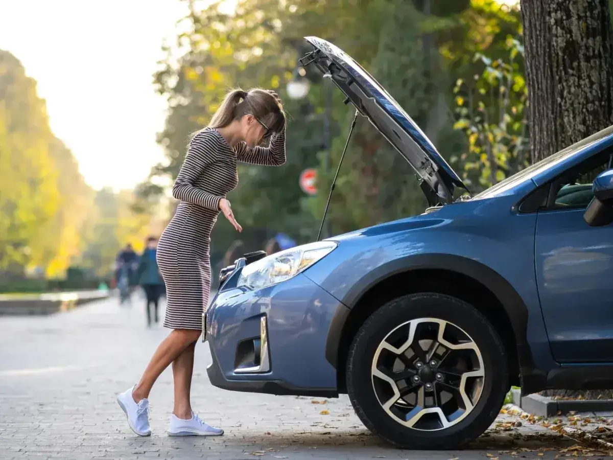 Kobieta zmartwiona patrzy pod maskę auta, szukając przyczyn problemów. Czy to objawy awarii pompy paliwa?