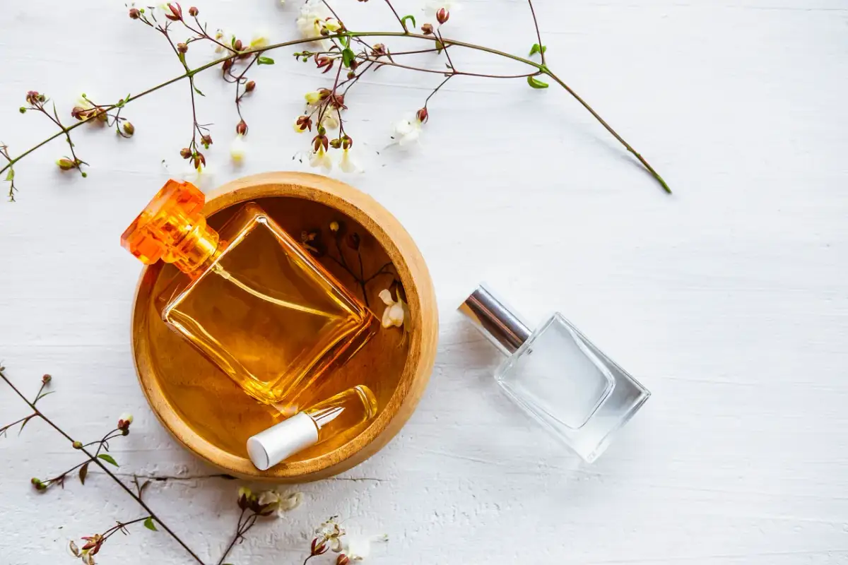 Dwie buteleczki perfum, jedna z bursztynowym płynem w drewnianej miseczce, druga szklana. Delikatne gałązki z kwiatami. Woda toaletowa ile alkoholu?