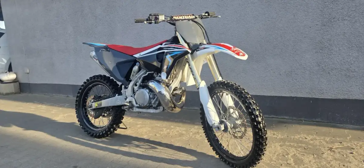 Motocykl crossowy Husqvarna CR 250 z czerwonym siedzeniem i czarnymi elementami, gotowy do jazdy po torze.