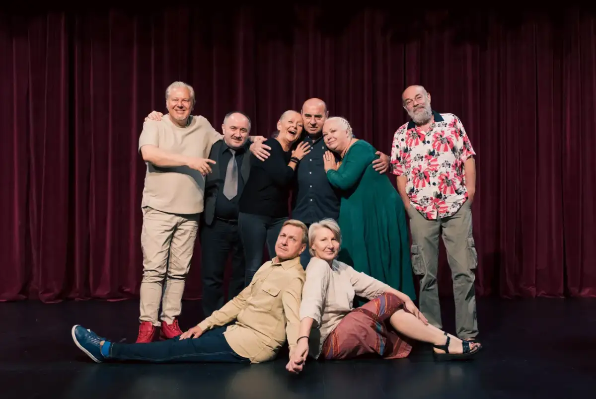 Aktorzy pozują na scenie przed bordową kurtyną. To zespół "Prywatna Klinika Spektakl", gotowy na kolejne przedstawienie.