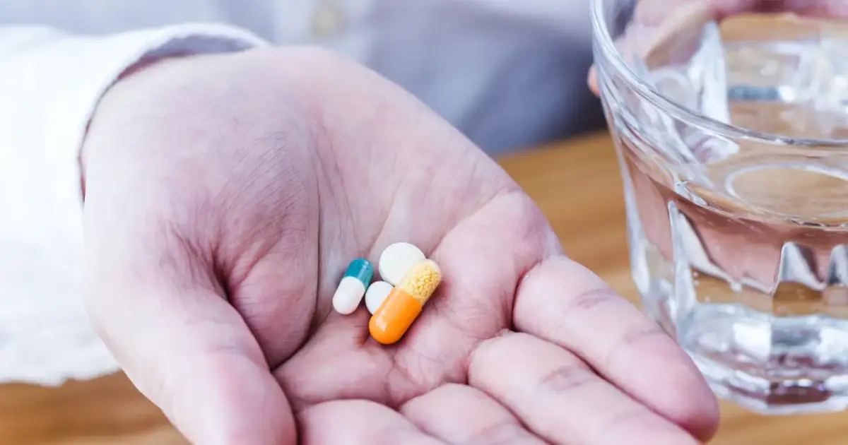 Dłoń z kilkoma tabletkami i kapsułkami, obok szklanka wody. Czy leki bez recepty można odliczyć od podatku?