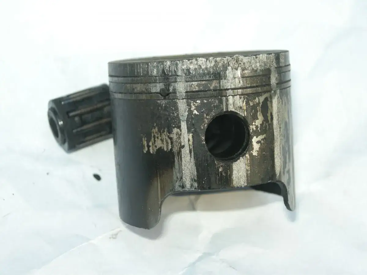 Zużyty tłok i sworzeń od kosy Husqvarna 125R, noszące ślady intensywnej eksploatacji.