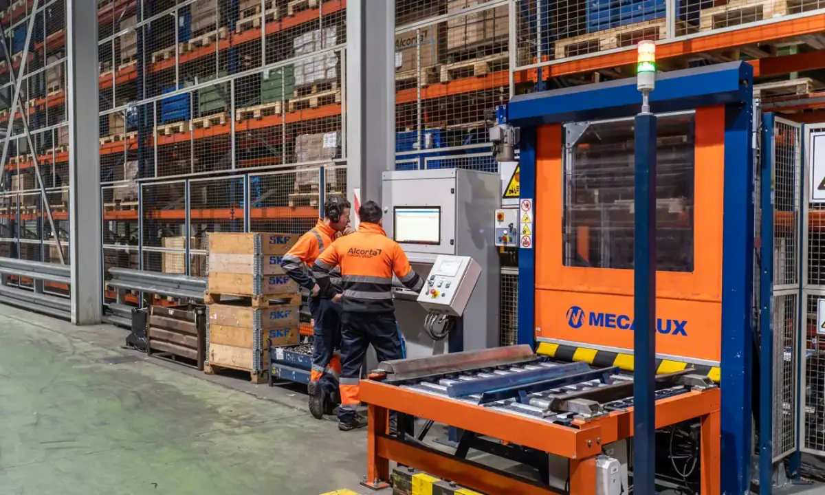 Dwóch pracowników w pomarańczowych kamizelkach obserwuje maszynę w magazynie. Zasada genchi genbutsu w praktyce – osobiście sprawdzają działanie sprzętu.