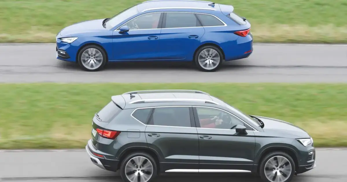 Dwa samochody klasy D: niebieskie kombi i ciemnoszary SUV, jadące obok siebie po drodze.
