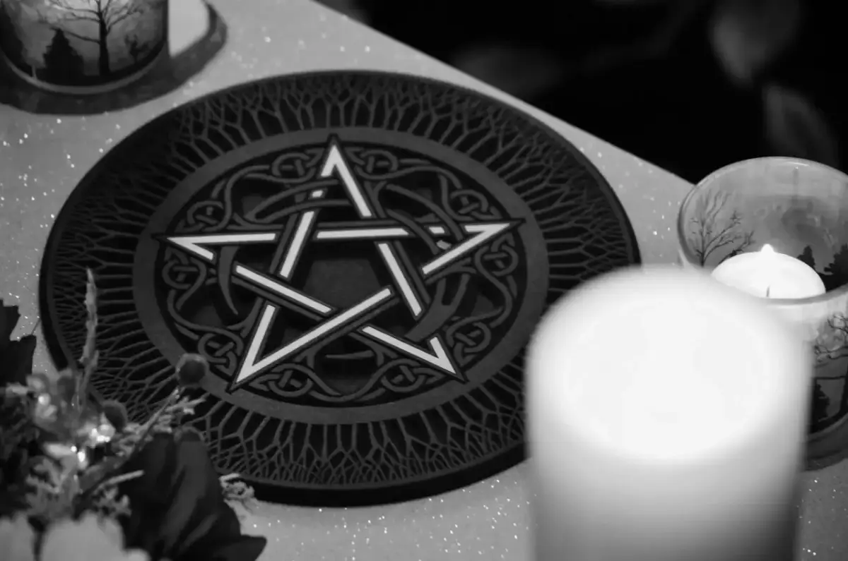 Oto jak wygląda pentagram: pięcioramienna gwiazda wpisana w okrąg, ozdobiona celtyckimi wzorami. Obok świeca w szklanym naczyniu.