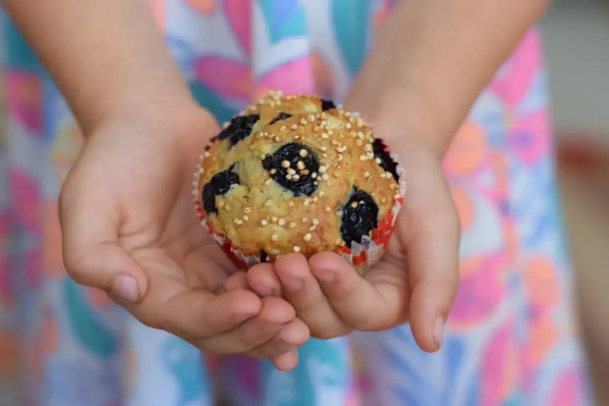 Dziecko trzyma w dłoniach pyszne muffinki z borówkami mrożonymi, posypane chrupiącym ziarnem.