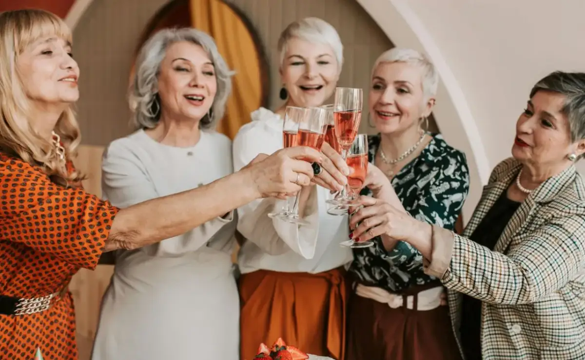 Pięć eleganckich kobiet wznosi toast kieliszkami z różowym winem. Idealne śmieszne życzenia na 70 urodziny dla mężczyzny!