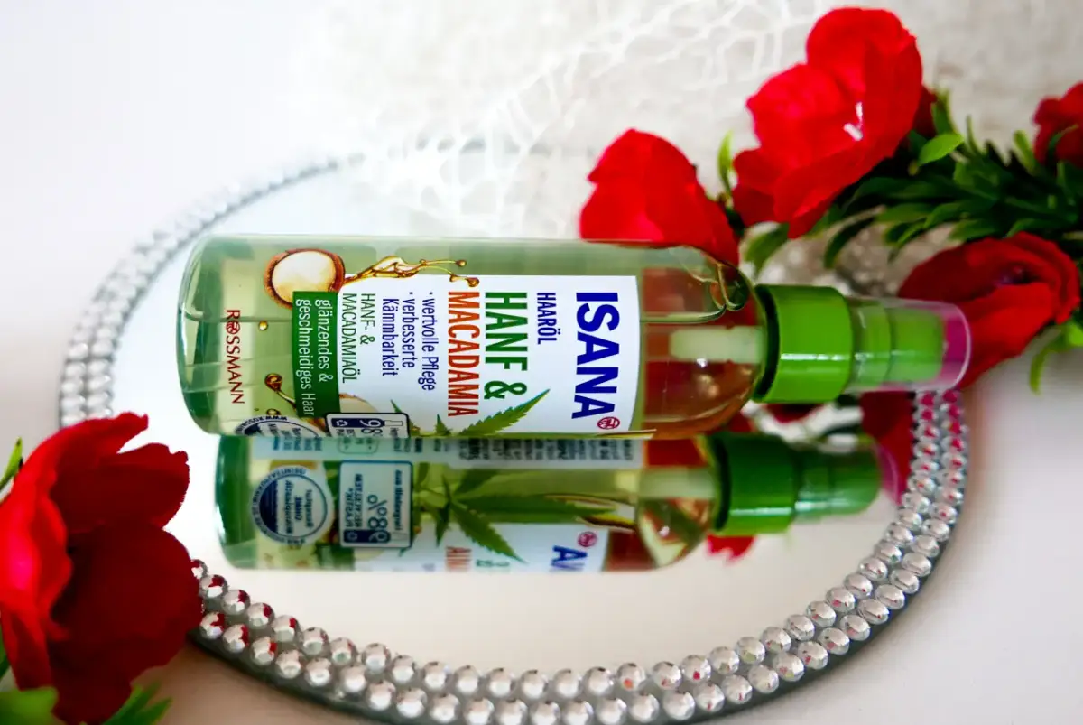 Butelka olejku do włosów Isana Hanf & Macadamia na lustrzanej tacy, otoczona czerwonymi kwiatami.