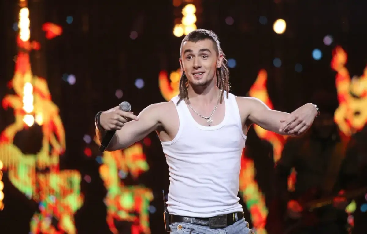 Kamil Bednarek w białej podkoszulce śpiewa na koncercie.