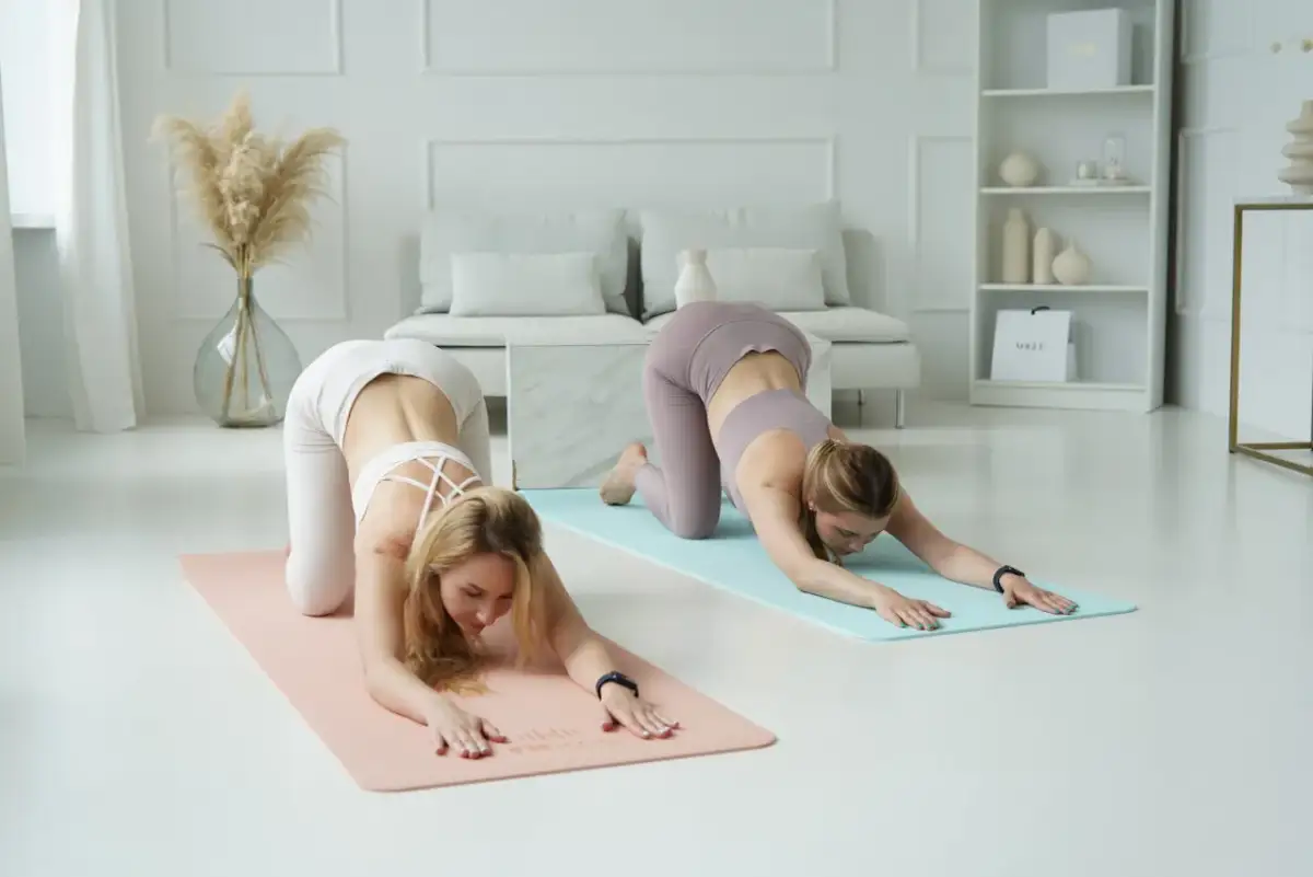 Dwie kobiety ćwiczą jogę w pozycji dziecka na matach w jasnym, minimalistycznym wnętrzu.