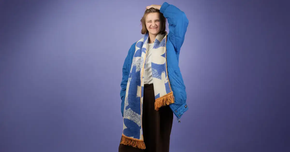 Dziewczyna w niebieskiej kurtce z kapturem i wzorzystym szaliku. Pokazuje, jak nosić szalik do kurtki z kapturem, tworząc stylowy look.