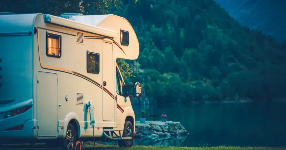 Kamper na kat B zaparkowany nad jeziorem, w tle góry porośnięte lasem.