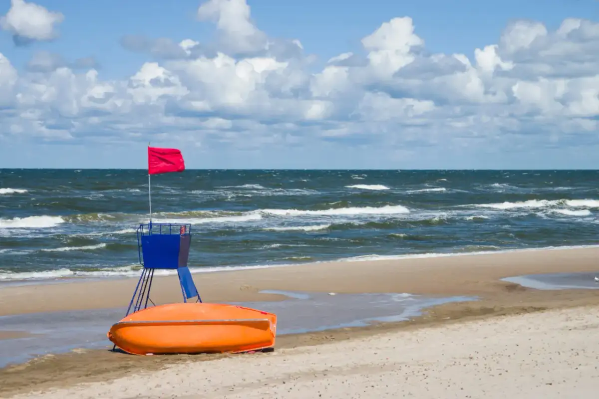 Ratownik z czerwoną flagą i łodzią ratunkową na plaży nad wzburzonym Bałtykiem.