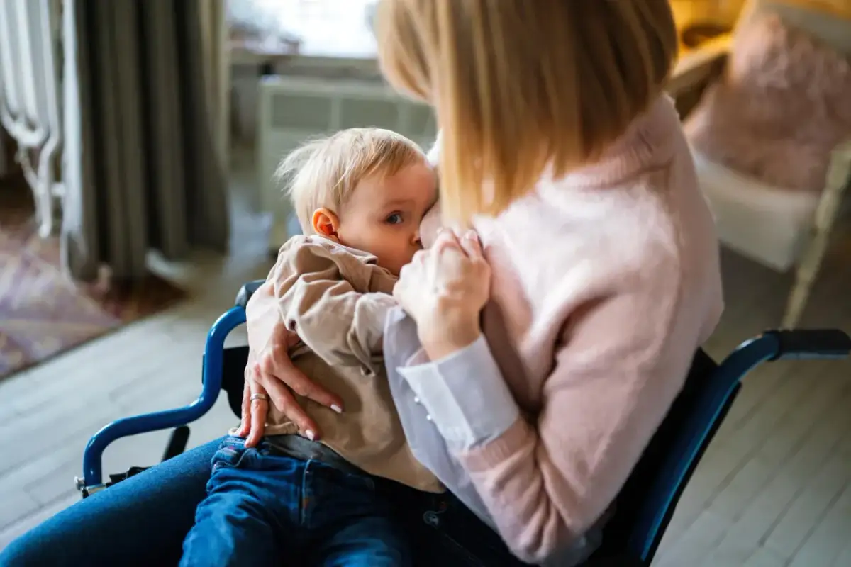 Mama w wózku inwalidzkim karmi piersią dziecko. To ważny moment, który może być częścią procesu, jak odstawić dziecko od piersi.