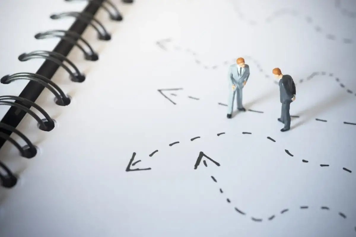 Figurki biznesmenów analizują ścieżki na mapie, symbolizujące bariery wejścia na rynek i strategie ich pokonywania.