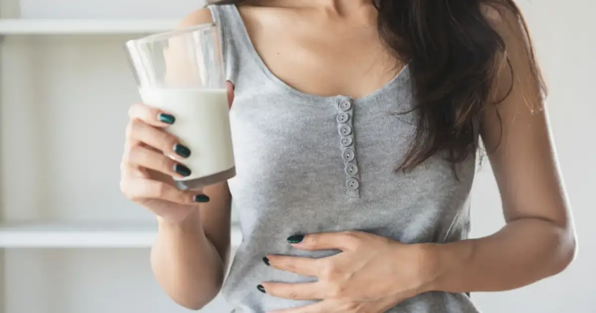 Kobieta z bólem brzucha trzyma szklankę napoju, zastanawiając się, czy mleko sojowe ma laktozę.