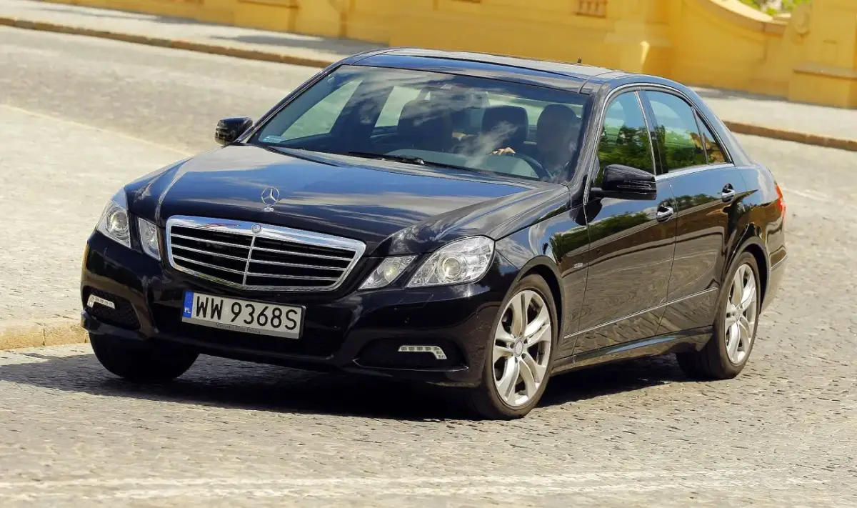 Elegancki, czarny Mercedes-Benz Klasa E porusza się po brukowanej ulicy.