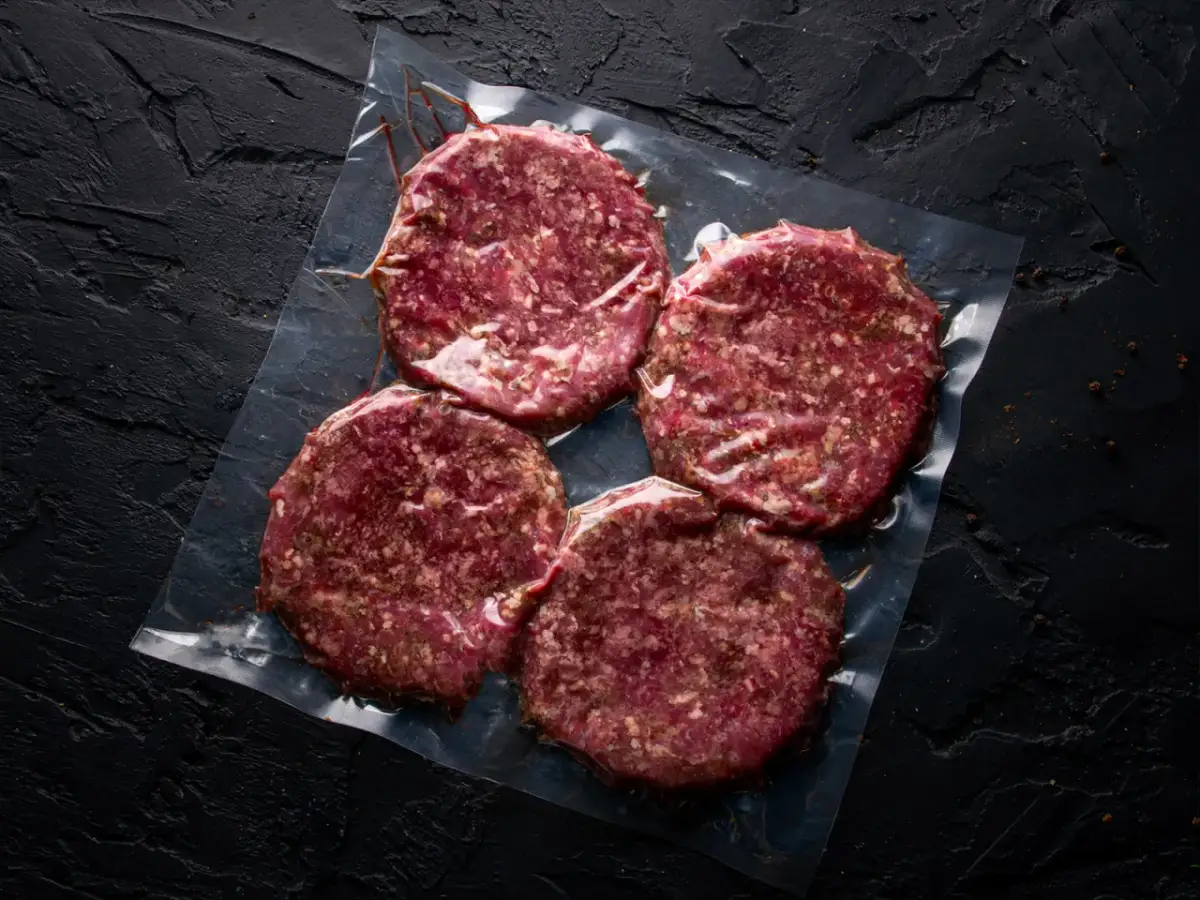 Cztery surowe kotlety na hamburgery w folii. Zastanawiasz się, mięso na hamburgery jak przyprawić?