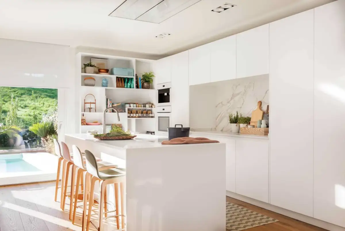 Elegante mueble cocina isla blanco con taburetes, encimera de cuarzo y vistas a un jardín con piscina.