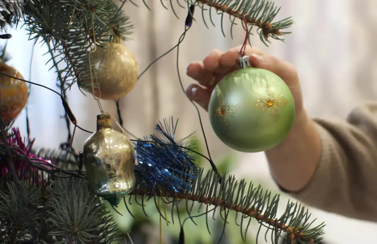 Ręka zdejmuje zieloną bombkę z choinki. Czas pomyśleć, kiedy ściągnąć dekoracje świąteczne.