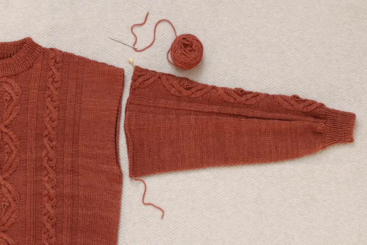 Części swetra robionego na drutach, igła i nitka czekają, by pokazać, jak zszyć sweter robiony na drutach.