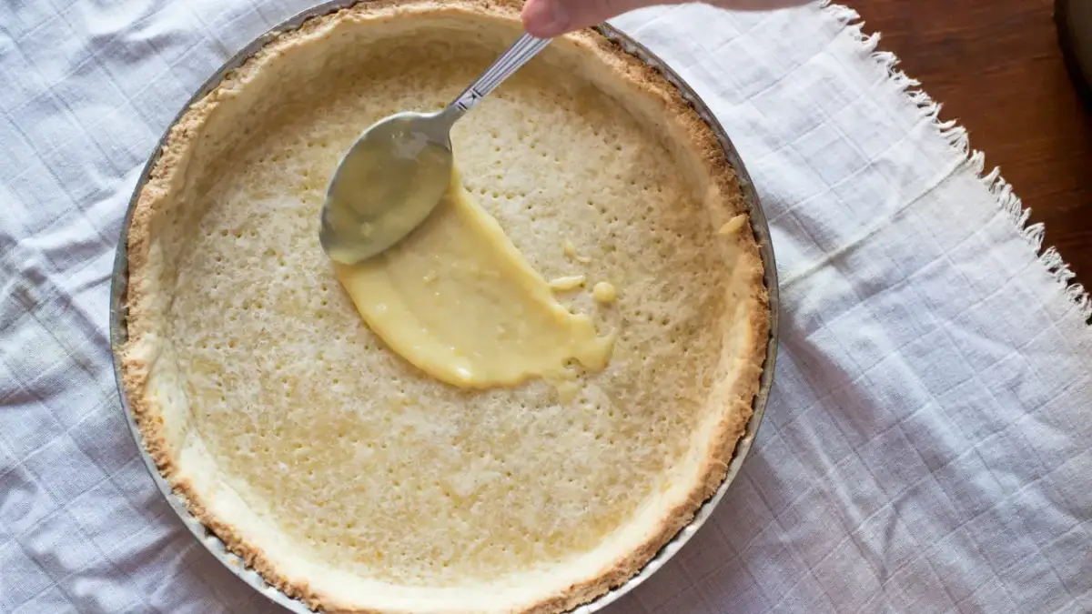 Łyżka rozprowadza krem cytrynowy na upieczonym spodzie. Idealny kruche ciasto przepis na pyszny deser.