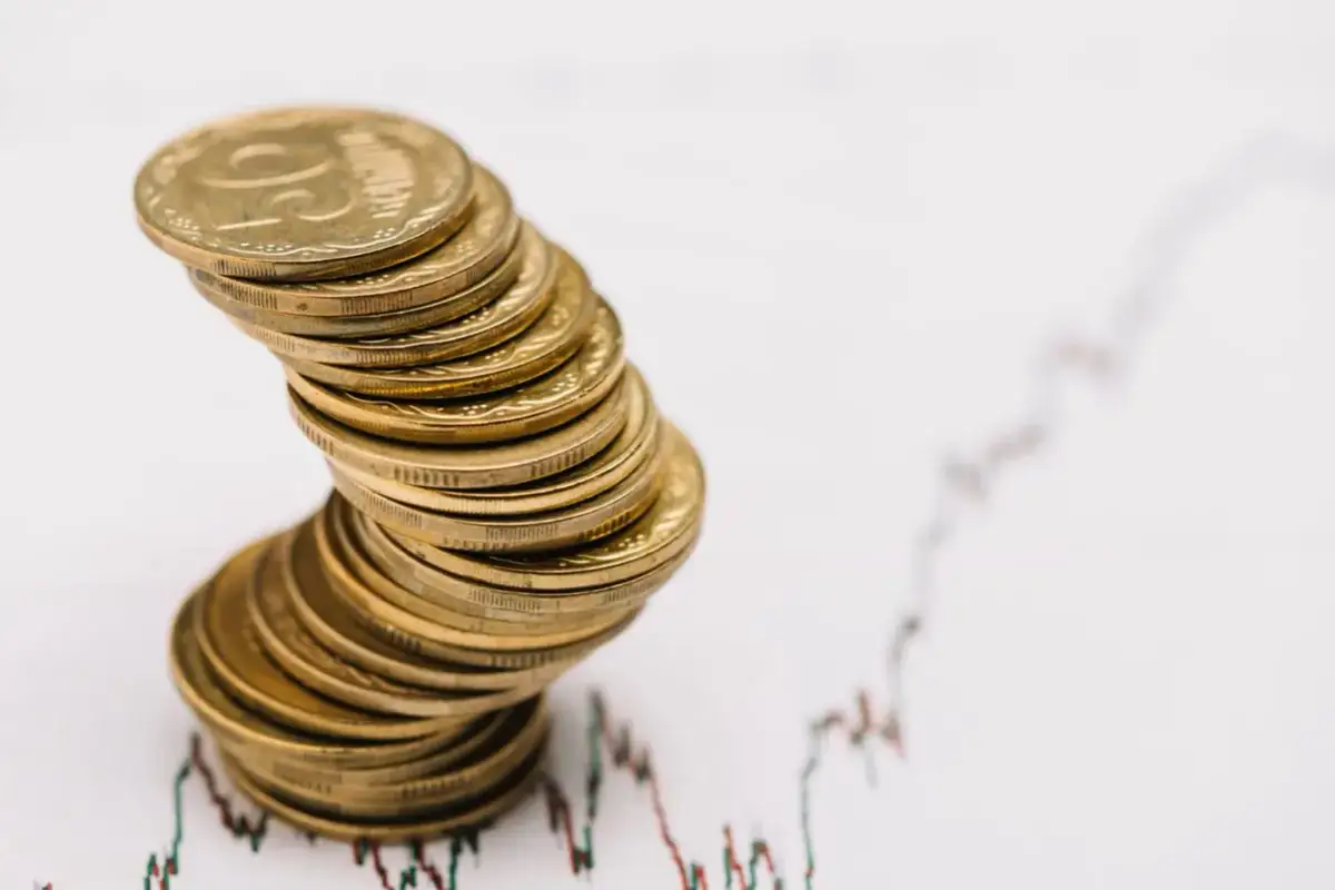 Stos monet złotych przechylony na tle wykresu giełdowego.
