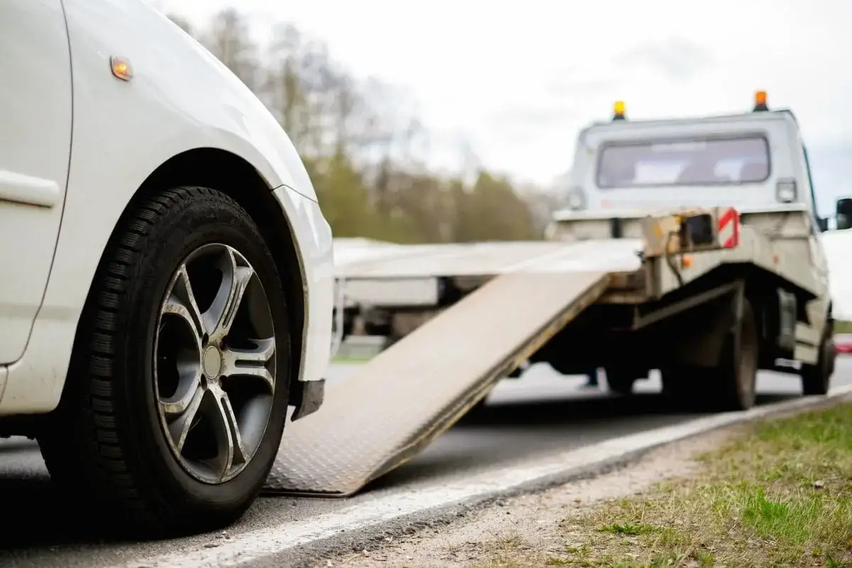 Białe auto na lawecie. Wygląda na to, że to szkoda całkowita w leasingu, auto jest zabierane przez pomoc drogową.