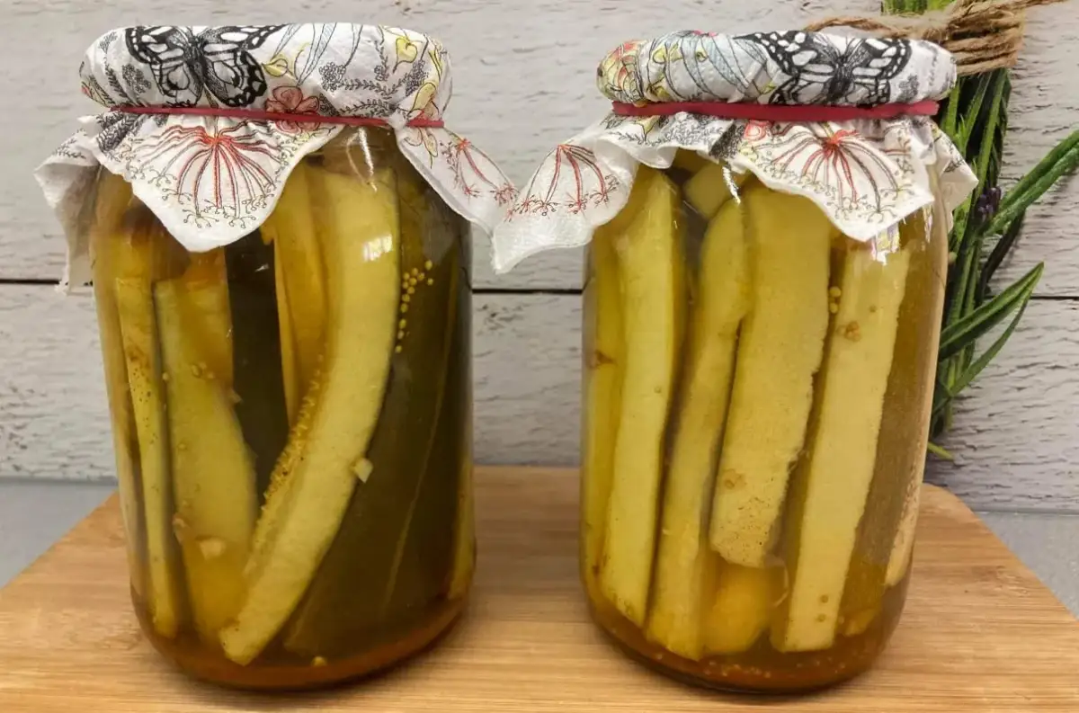 Dwa słoiki z cukinią w zalewie słodko-kwaśnej z curry. W tle gałązka rozmarynu.