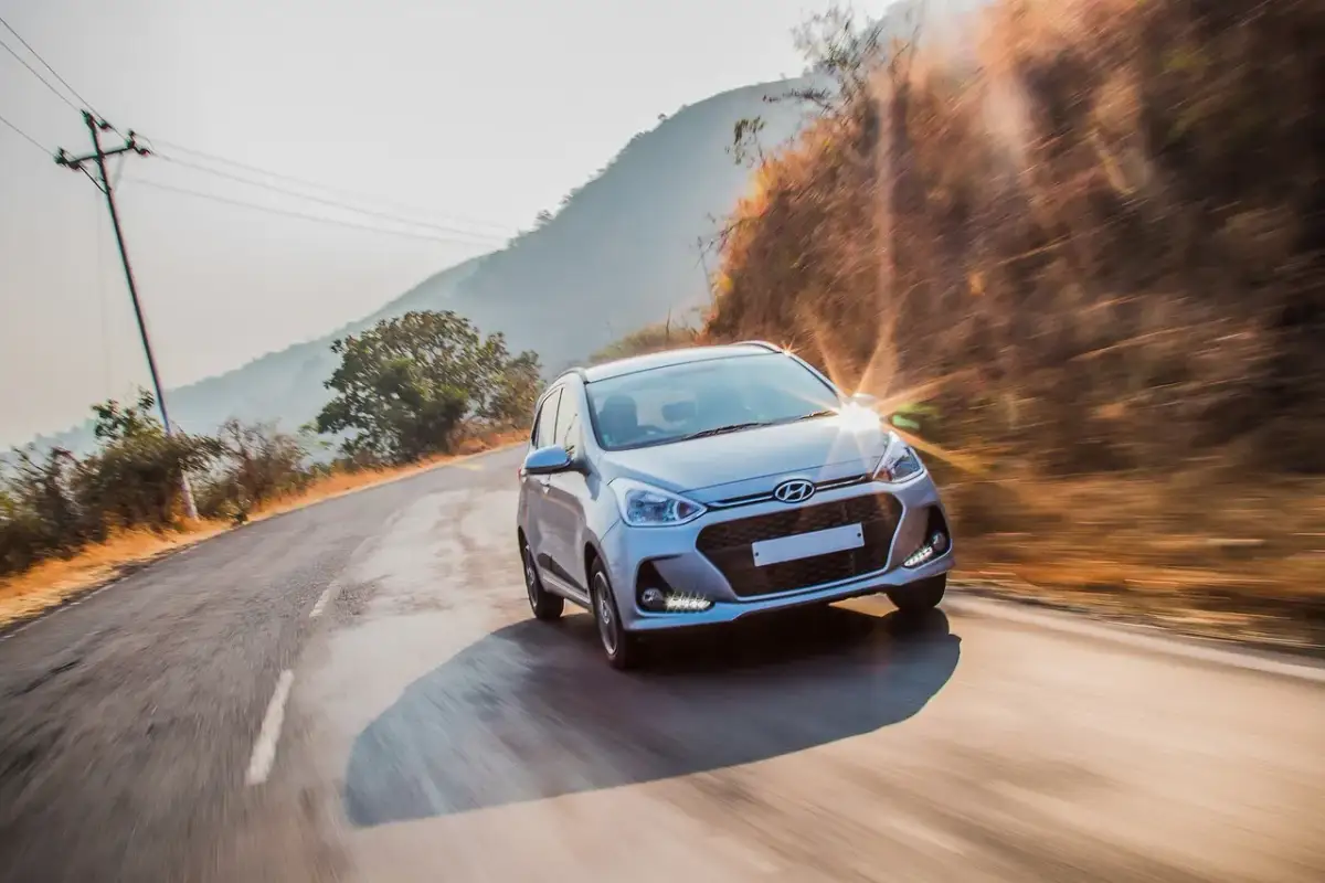 Srebrny Hyundai przemierza krętą drogę w słoneczny dzień. Ten Hyundai z jakiego kraju pochodzi? Z Korei Południowej, gdzie powstała ta marka.