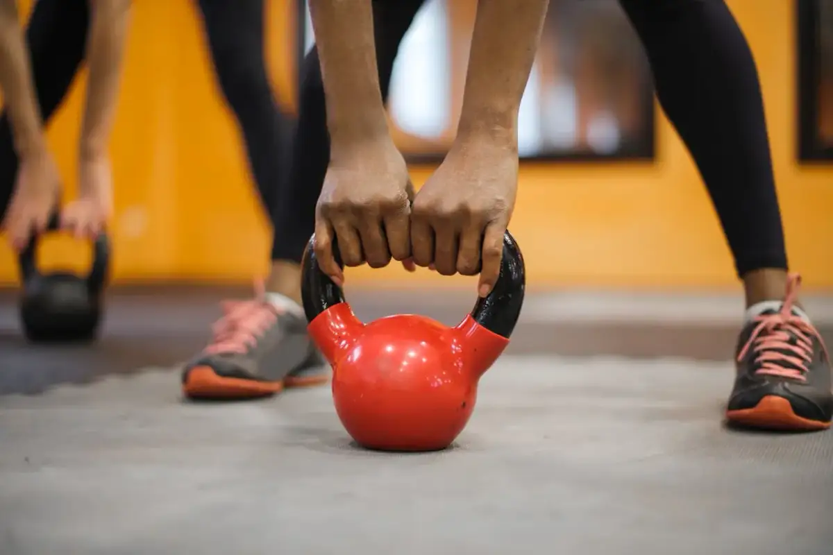 Dłonie trzymające czerwoną kettlebell na siłowni.